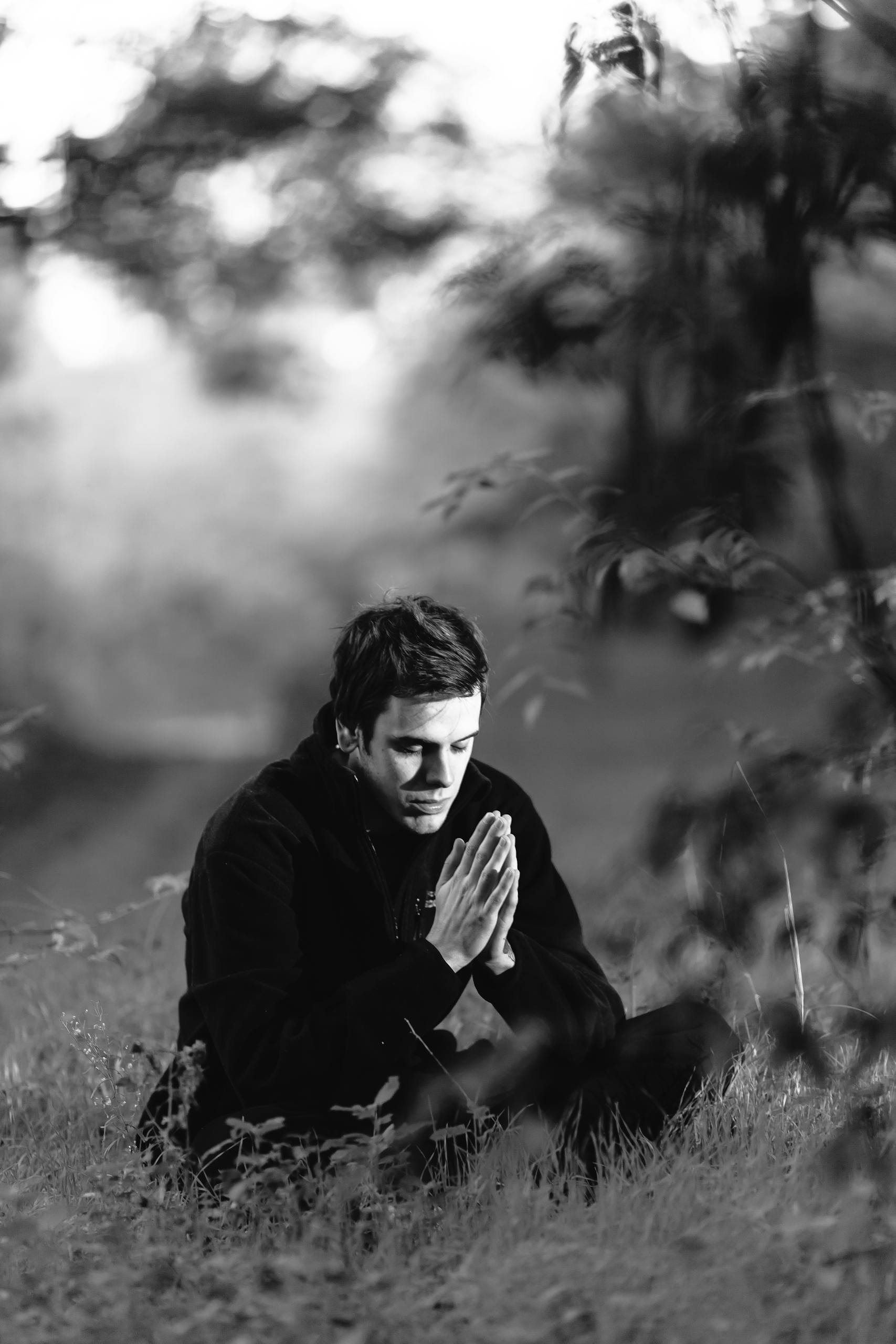 Grayscale Photography of Man Sitting on Grass Field